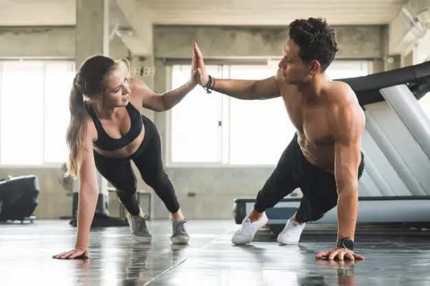 Mulher e homem batendo as mãos durante um treino na academia
